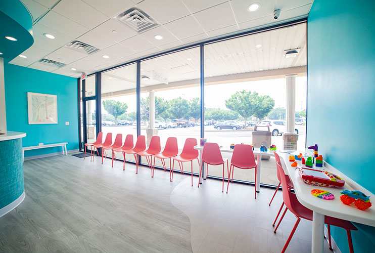 The Little Molars waiting room with pink chairs and a play table by large windows